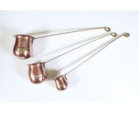 Set of three copper spirit measures for whisky, rum and brandy, on long brass hanging handles, largest 38cm long