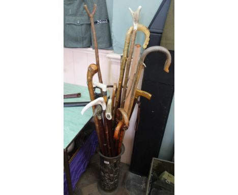 A large collection of various walking sticks (some bespoke) and two shooting sticks, all within brass stick stand