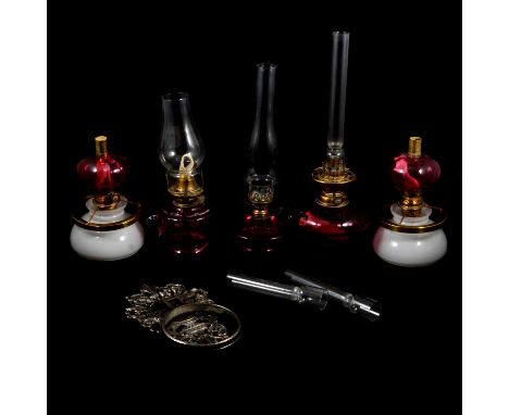 Pair of cranberry tinted brass column peg lamps, with opaque glass shades, 23cm high; two further oil lamps with cranberry ti