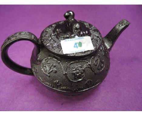 A 19th century black pottery teapot having lion finial embossed scroll floral decoration