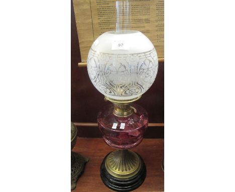 Early 20th century double oil burner lamp having frosted and etched globular shade cranberry reservoir on a brass and ebonise