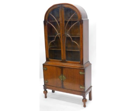 An Art Deco oak display cabinet, with an arched top, two astragal glazed doors enclosing three shaped shelves, the base with 