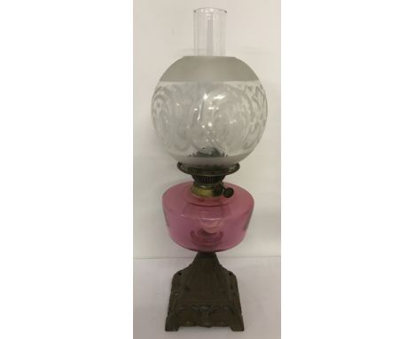 An Edwardian oil lamp with cast iron decorative base and cranberry coloured glass bowl. Complete with chimney and etched clea