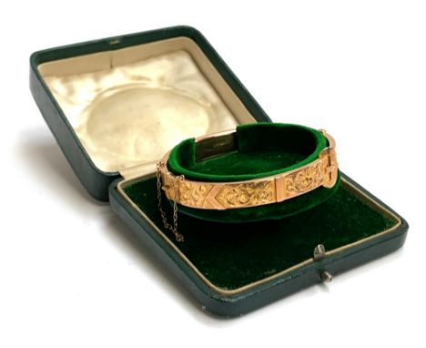 An Edwardian 9ct gold bangle of buckle form, foliate engraved decoration, with safety chain, hallmarked for Birmingham 1910, 