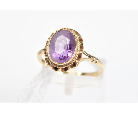 A 9CT GOLD AMETHYST RING, the oval amethyst within a collet setting with rope twist and undulating surround to the bifurcated