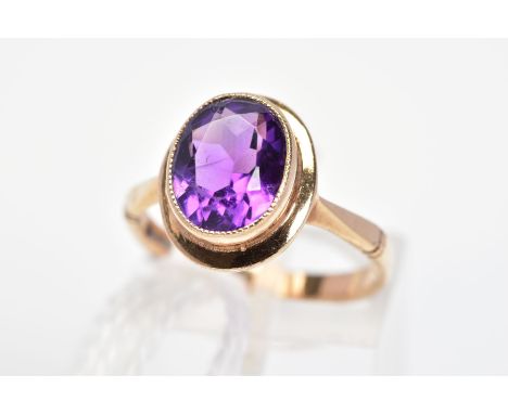 A 9CT GOLD AMETHYST RING, the oval amethyst in a millegrain setting to the plain surround and tapered shoulders, with 9ct hal