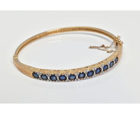 A 9CT GOLD SAPPHIREM AND DIAMOND HINGED BANGLE, designed as a line of eleven circular sapphires interspaced by single cut dia