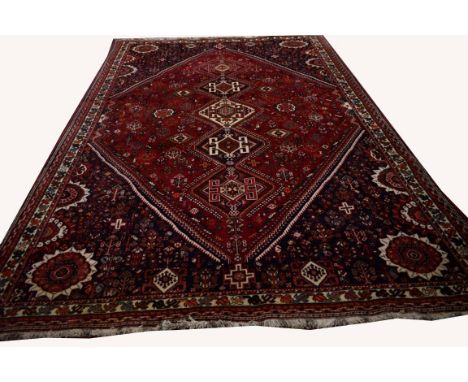 A BURGUNDY GROUND ORIENTAL CARPET, with three diamond shaped medallions inside an all-over stylised floral field within dark 