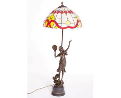 AN ATTRACTIVE TIFFANY STYLE BRONZE TABLE LAMP, modelled with a woman and tambourine, with coloured and metal shade, on a circ