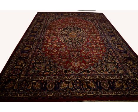 A FINE PERSIAN MASHAD CARPET, the burgundy ground with all-over floral pattern and large centre medallion, inside a wide dark