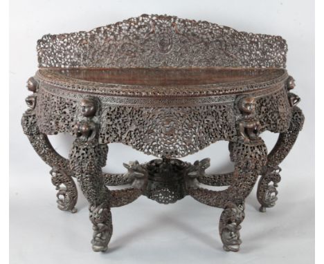 A 19th century Burmese carved hardwood console table, of demi-lune form, carved and pierced with birds and fruit, leopards an