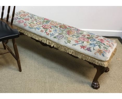 An early 20th Century walnut framed long stool with tapestry seat on acanthus carved cabriole legs to lion's paw feet, 122 cm