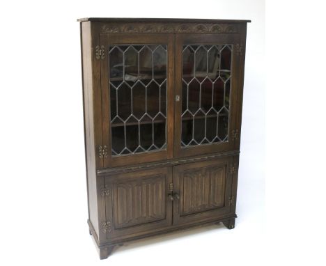 A stained oak glazed bookcase. Circa 1920, the double glazed astragal doors enclosing two shelves above double linenfold patt