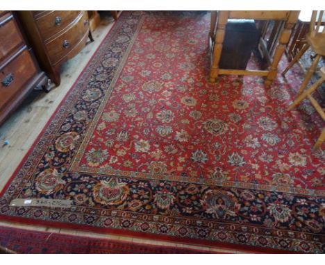 A 20th century machine made large carpet, decorated throughout with stylized floral swags on a red ground, within blue border