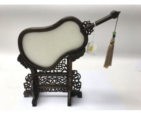 A jade handscreen on a carved wooden stand.