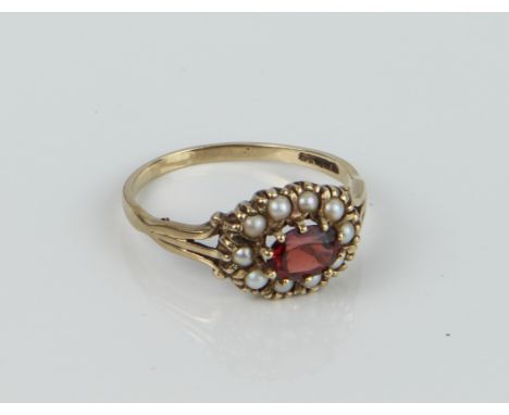 A 9ct yellow gold, garnet and seed pearl cluster ring - hallmarked Birmingham 1989, the oval cut garnet within a border of se