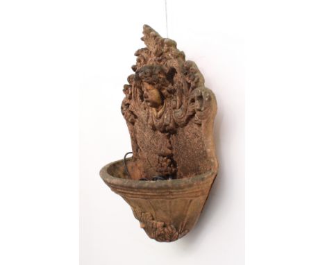 A terracotta coloured composite stone garden wall-mounted water fountain - with mask, foliate scroll, floral and grape decora