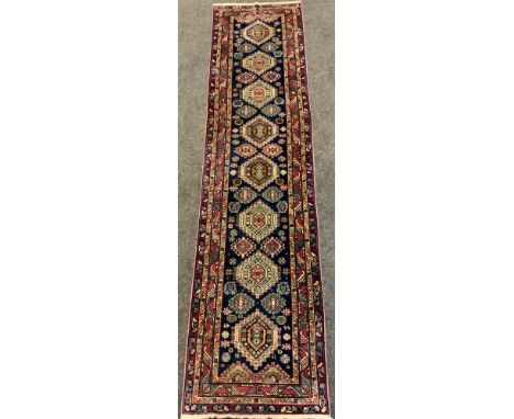A hand-made Heriz runner carpet, woven with stylised geometric motifs in shades of red, pale green, and deep blue, 345cm x 85