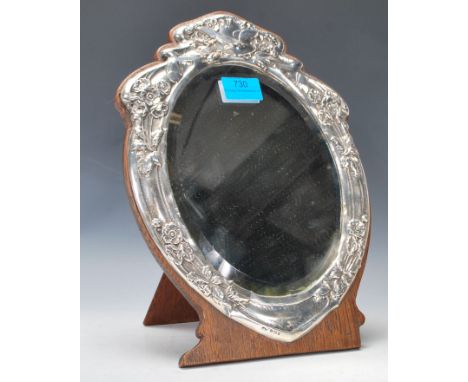 An early 20th Century silver mounted Art Nouveau shield shaped easel mirror having embossed silver surround decorated with fl