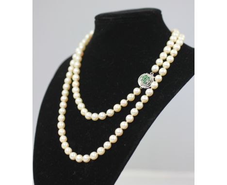 A single strand uniform cultured pearl necklace, each pearl of approximately 7mm diameter, with attached white metal, emerald