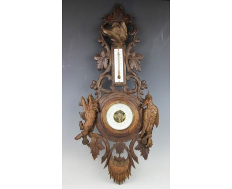 A 19th century Black forest barometer, carved with scrolling vines, a wild boar, woodpecker and hound with inset thermometer,