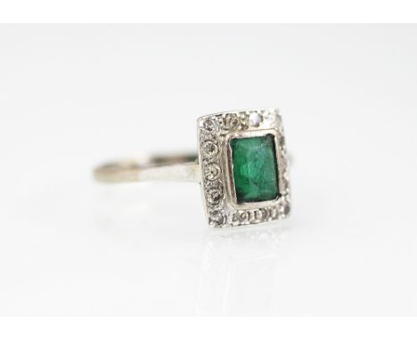 A diamond and emerald Art Deco style ring, the central emerald within a diamond set surround, all set in white metal to the p