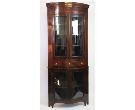 An Edwardian inlaid mahogany bow front corner display cabinet, with moulded cornice and two glazed doors, over two further dr