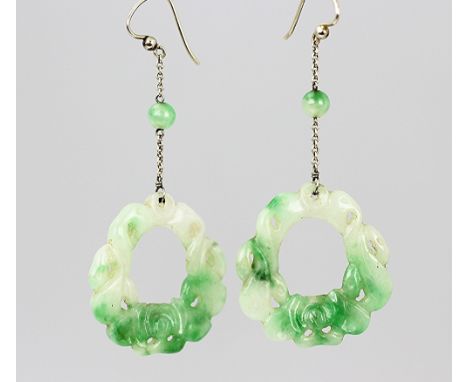 A pair of carved jade drop earrings, each designed as a circular carved drop, suspended from a fine chain and with white meta