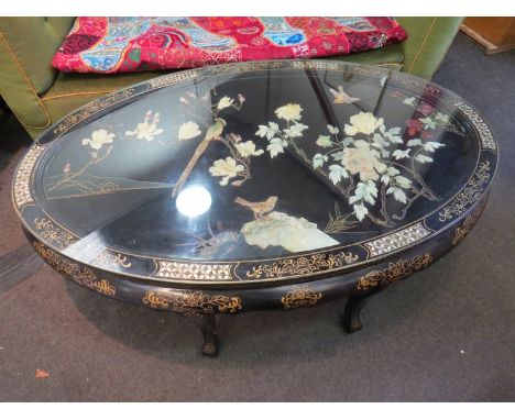 A 20th Century oriental lacuered oval coffee table with mother of pearl and gilt border, cental high relief image of birds an