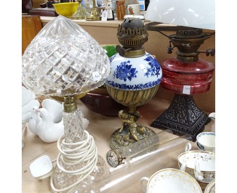 A Victorian blue and white porcelain oil lamp, with brass cherub support, a Victorian oil lamp with cranberry glass font, hei