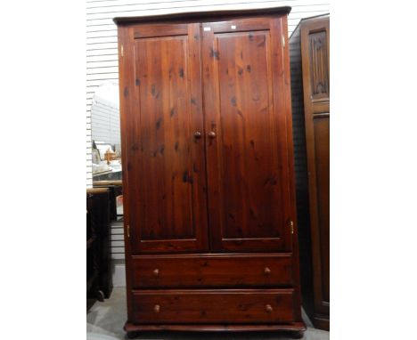 Stained pine wardrobe, the pair panel doors enclosing shelf and hanging space, two long drawers below, width 104cm 