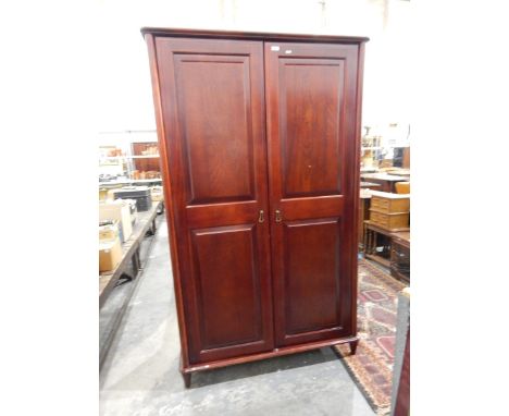 Contemporary double wardrobe the panel doors enclosing shelf and hanging space, raised on turned legs, width 110cm 