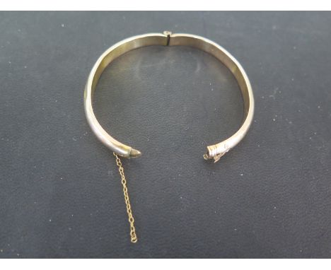 A 9ct yellow gold hinged bangle with safety chain attached to one side only - gross weight approx 8.9 grams - dented