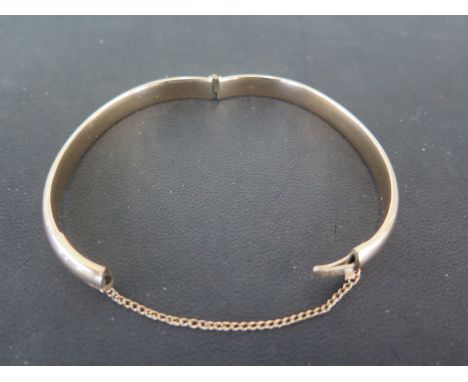 A 9ct yellow gold hinged bangle with attached safety chain - in good condition - weight approx 40 grams