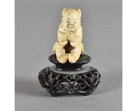 A Japanese Meiji period ivory carved netsuke, modelled as a seated boy inspecting his clasped hands, 3.5 cm wide 