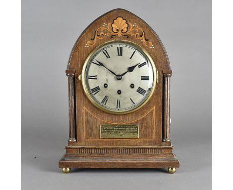 An Edwardian oak and inlaid eight day mantel clock, of arched form with steel face and roman numerals, presentation plaque wi