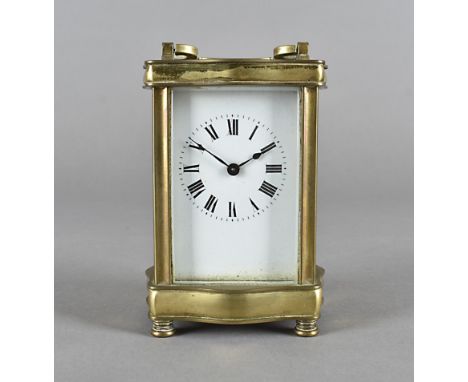 An early 20th century brass carriage time piece, shaped outline, white enamel face and Roman numerals, 13 cm high  