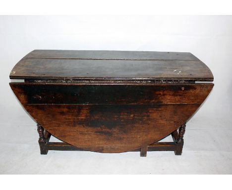 An 18th century oak long drop gate leg table on early refectory style base, with end drawer oval top supported on turned supp