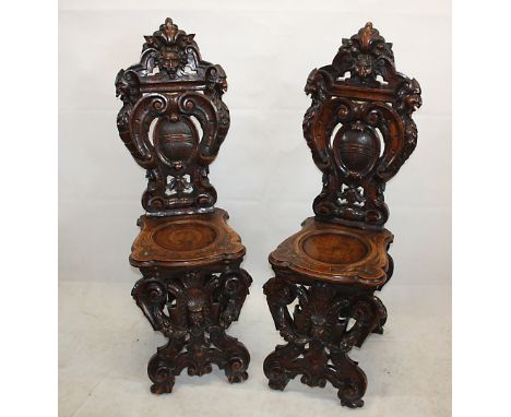 A pair of 19th Century continental walnut carved hall chairs, with mask and scroll carved backs, poker work seats and carved 