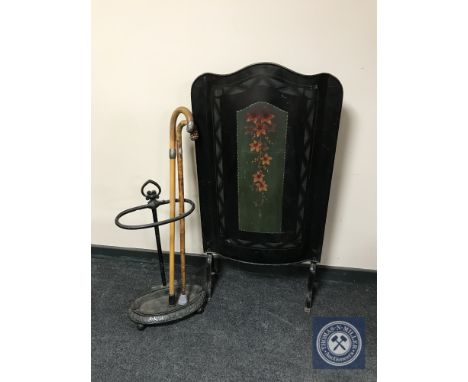 A 20th century hand painted fire screen together with a cast stick stand containing sticks, parasols etc