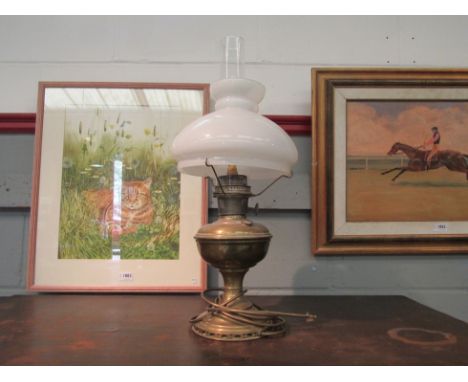 A brass oil lamp with a clear chimney and white opaque shade and a brass framed mirror 