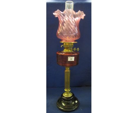 Early 20th Century brass double burner oil lamp with cranberry glass reservoir on a brass pedestal with ceramic base, wrythen