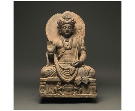 100-300 AD. Gandharan. Schist figure of a bodhisattva, backed by a halo, who sits, gazing serenely into the distance. He is d