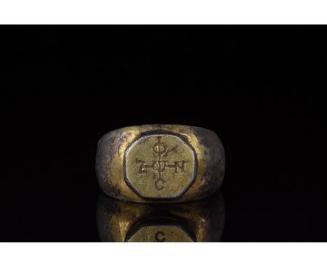 1100-1300 AD. Byzantine. A silver gilt ring with a round hoop and octagonal trumpet bezel engraved with a Greek cross monogra