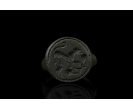 100-200 AD. Roman. A rare bronze ring with a circular hoop and round plate bezel bearing an engraved scene of a lion (left) a