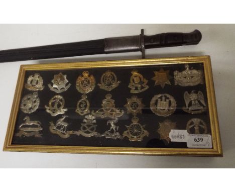 A Remington bayonet, 1913, with scabbard, and a group of cap badges, framed (2)