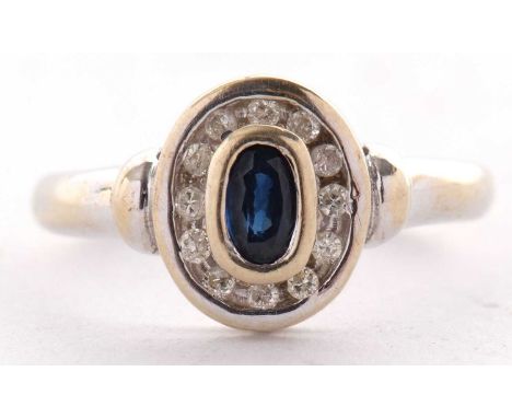 An 18ct sapphire and diamond ring, the collet mounted oval sapphire surrounded by a ring of channel set small round diamonds,