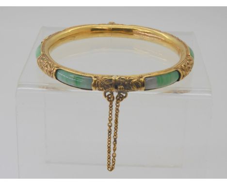 AN ORIENTAL BANGLE made in bright yellow metal chased with different plants and flowers and set with Chinese green and white 