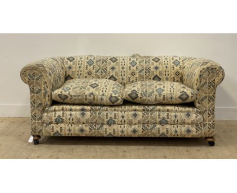 A late Victorian chesterfield two seat sofa, with squab cushion, and upholstered in geometric patterned cotton, raised on com