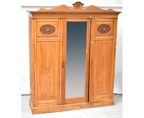 An Edwardian satin walnut triple wardrobe, the shaped cornice centred with a carved roundel above a central mirrored door wit